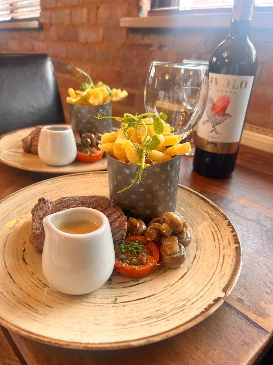 Steak with grilled tomato, mushrooms and a jug of sauce, chips on the side